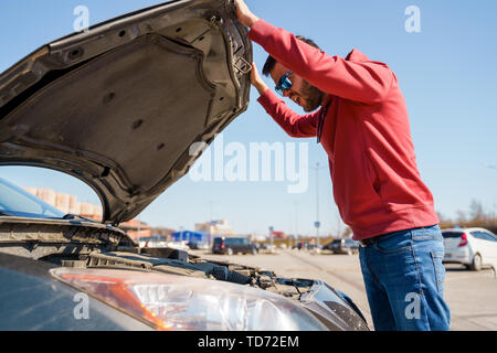 Bild von Seite der Mann mit Brille Nächster Haube der gebrochenen Auto zu öffnen während der Tag Stockfoto