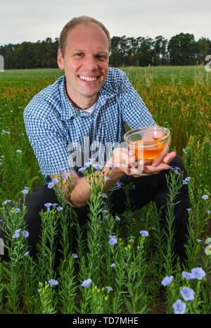 Schlepzig, Deutschland. 13. Juni, 2019. Christian Behrend, Inhaber der Kanow Mühle, zeigt eine Schüssel mit Leinöl während einer Pressekonferenz auf der Öllein blühen auf ein Feld der landwirtschaftlichen Genossenschaft "unterspreewald". Öl Flachs ist eine alte Kulturpflanze, die für Faser- und Ölproduktion angebaut wird. Die landwirtschaftliche Genossenschaft "unterspreewald" aus Dürrenhofe wächst Öllein auf einer Fläche von über 30 Hektar in diesem Jahr. Im gesamten Spreewald Die zarte blau blühende Pflanzen wachsen in diesem Jahr auf einer Fläche von 210 Hektar. Foto: Patrick Pleul/dpa-Zentralbild/ZB/dpa/Alamy leben Nachrichten Stockfoto