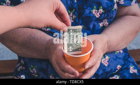 Alte Frau bittet um Almosen. Nahaufnahme von Geld und Münzen in der Hand der armen Frau. Die sozialen Probleme der Gesellschaft Stockfoto