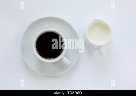 Tasse mit Untertasse Espresso Kaffee und einen kleinen Krug mit Milch auf weißem Hintergrund. Ansicht von oben. Schließen Sie herauf Bild. Stockfoto