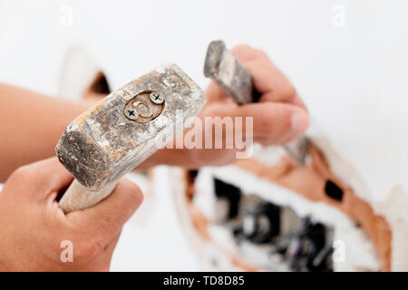 Nahaufnahme der kaukasischen Mann, der ein Loch in einem verputzten Backsteinmauer mit einem Hammer und einem kalten Meißel Stockfoto