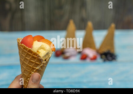 Süßes Eis in Kugeln auf einem Holz- Hintergrund. Dessert mit verschiedenen Aromen und frische Beeren und Früchte. Eis in der Waffel Kegel. Platz kopieren Stockfoto