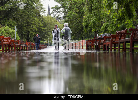 Menschen laufen über einen Fußweg in Edinburghs Princes Street Gardens, die Aufgrund der schwere Regen überschwemmt haben, wie Meteorologen glauben, dass sich das Wetter eingestellt ist zu verbessern, wird nach "verräterische" Bedingungen in Teilen des Landes nach intensiven Regenfällen und Überschwemmungen. Stockfoto