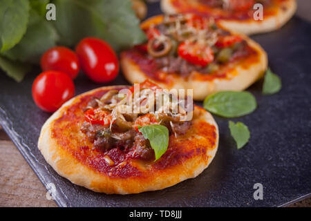 Mini Pizza belegt mit Schinken, grüne Oliven, Tomaten und frischem Basilikum. Hausgemachte Speisen. Konzept für einen leckeren und herzhaftes Essen. Close Up. Stockfoto