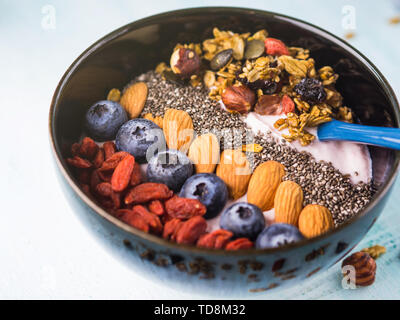 Joghurt Himbeer smoothie Schüssel mit Goji Beeren und Heidelbeeren, Mandeln, Chia Samen und Müsli auf Pastell türkis Holz- Hintergrund. Anlage b Stockfoto