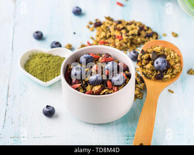 Hausgemachte Matcha Grüntee Müsli in Schüssel auf Pastell türkis Hintergrund. Hafer Müsli mit Goji Beeren, getrocknete Früchte, Samen und Nüsse. Gesunde Frühst Stockfoto