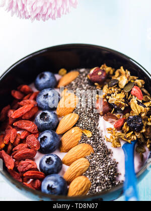 Joghurt Himbeer smoothie Schüssel mit Goji Beeren und Heidelbeeren, Mandeln, Chia Samen und Müsli auf Pastell türkis Holz- Hintergrund. Anlage b Stockfoto