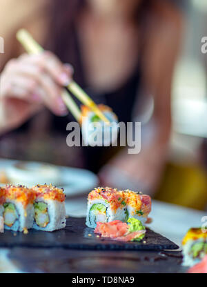 Sushi essen im Restaurant, eine Frau mit Stäbchen nimmt ein Stück von Roll, genießen Sie leckeres und gesundes Essen, traditionelle asiatische Küche Stockfoto
