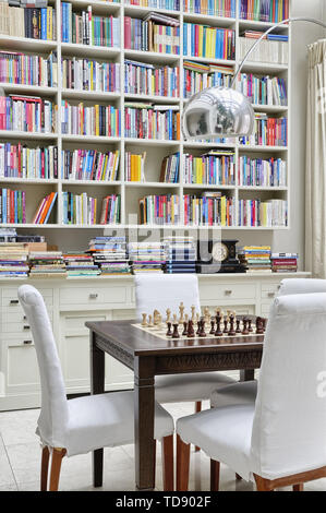 Dunkelbraun schach Tabelle mit weißen Stühlen vor der hängenden Bücherregal über Kommode in der Orangerie des VEREINIGTEN KÖNIGREICHS UND IRLANDS NUR RECHTE Stockfoto