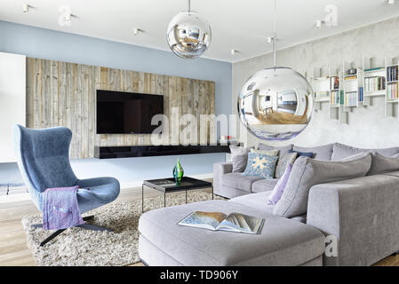 Moderne eklektische Wohnzimmer mit bequemen grauen sectional Sofa, Metall schwarz Tray Table und rustikalen hölzernen Wand Großbritannien & Irland NUR VERWENDEN Stockfoto