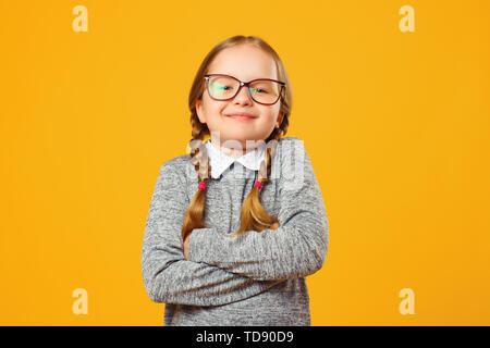 Closeup Portrait von ein fröhliches kleines Mädchen in Gläsern auf gelben Hintergrund. Kind Schulmädchen faltete ihre Arme und sieht in die Kamera. Stockfoto