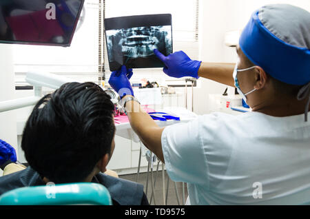 Zahnarzt Arzt bleibt in den Händen von X-ray Bild des menschlichen Kiefers, es analysieren mit dem Patienten und der Krankenschwester Stockfoto