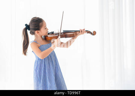 Süße Mädchen spielen Geige in Weiß Schlafzimmer mit weißen Vorhang Hintergrund. Musikalische und Lebensstile. Freizeit und Bildung Konzept. Zurück zur Scho Stockfoto