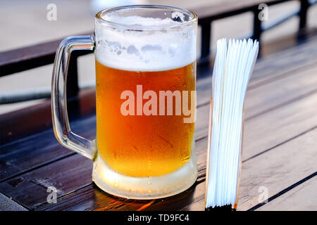 Eine Tasse kaltes Bier, beschlagenen Tröpfchen auf dem Glas. Auf dem Tisch neben dem serviettenhalters mit Servietten Stockfoto