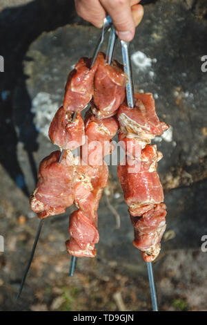Mann hält in der Hand einen Spieß mit rohem Fleisch, Life Style. Stockfoto
