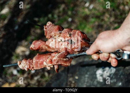 Mann hält in der Hand einen Spieß mit rohem Fleisch, Life Style. Stockfoto