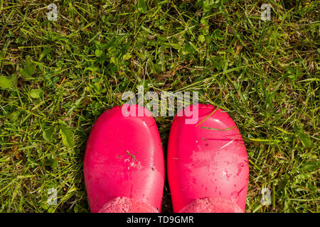 Auf der Suche nach rosa Schuhe Gummi auf Gras. Frau in Gummistiefel wandern im Regen. Mädchen mit rosa regen Stiefel außerhalb. gumboots auf Rasen. Kopieren Stockfoto