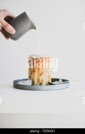 Des Menschen Hand gießen Milch zu Glas Caramel Macchiato Stockfoto