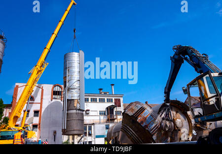 Lader Maschinen mit hydraulischer grappling Klaue und Kran sind die heavy metal Silo in industriellen Komplexes. Stockfoto