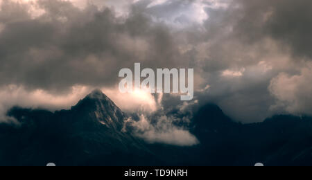 Die Sonne scheint auf die Gipfel durch die Wolken. Stockfoto