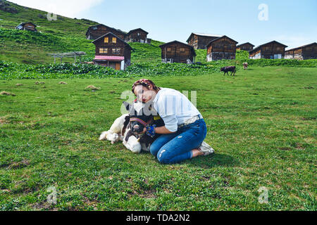 Ein Mädchen umarmt vor Holzplateauhäusern die Babykuh mit Liebe. Aufgenommen am Sal Plateau, Rize, Hochland der Nordosttürkei. Stockfoto