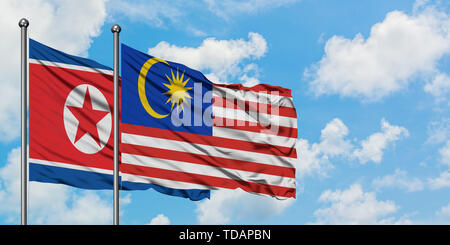 Nord Korea und Malaysia Flagge im Wind gegen Weiße bewölkt blauer Himmel zusammen. Diplomatie Konzept, internationale Beziehungen. Stockfoto