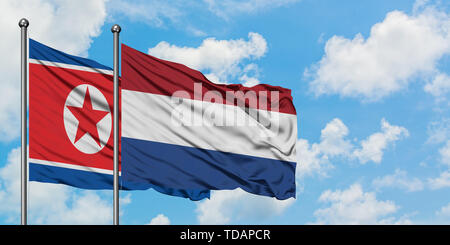 Nordkorea und die Niederlande Flagge im Wind gegen Weiße bewölkt blauer Himmel zusammen. Diplomatie Konzept, internationale Beziehungen. Stockfoto