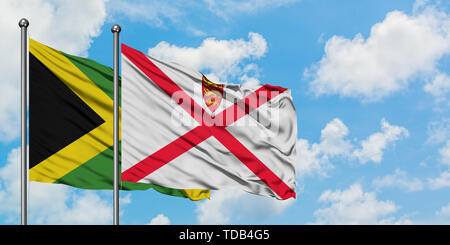 Jamaika und Jersey Flagge im Wind gegen Weiße bewölkt blauer Himmel zusammen. Diplomatie Konzept, internationale Beziehungen. Stockfoto