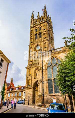 Menschen zu Fuß vorbei an der Stiftskirche St. Maria, Warwick, Warwickshire, Großbritannien. Der gotische Turm wurde im 18. Jahrhundert nach einem Brand wieder aufgebaut. Stockfoto