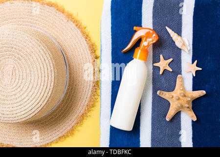 Strand flach Zubehör mit kopieren. Gestreifte blaue und weiße Handtuch, seashells, staw Sonnenhut und eine Flasche Sonnencreme auf gelben Hintergrund. Sommer Stockfoto