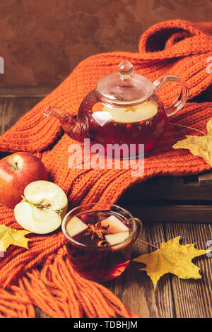 Trinken Herbst apple rote Beeren in eine Teekanne aus Glas und eine orangefarbene Schal auf einer hölzernen Hintergrund. Hot fruit Berry Tee. Stockfoto