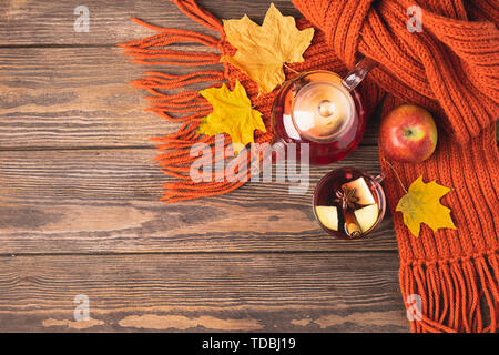 Trinken Herbst apple rote Beeren in eine Teekanne aus Glas und eine orangefarbene Schal auf einer hölzernen Hintergrund. Hot fruit Berry Tee. Stockfoto