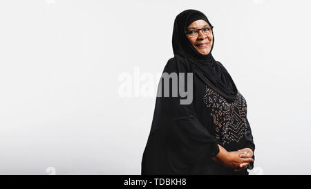 Ältere muslimische Frau im hijab auf weißem Hintergrund. Lächelnd arabische Frau in Brillen und Schwarz hijab an Kamera schaut. Stockfoto