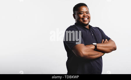 Starke afrikanische Mann gegen den weißen Hintergrund auf Kamera. Portrait von lächelnden afrikanischen Mann stand mit verschränkten Armen. Stockfoto