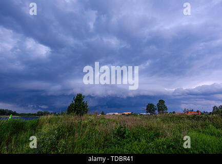 Gewitterwolken bilden über grüne Wiesen und Weiden durch den Fluss am 13. Juni 2019. Riga, Lettland Stockfoto