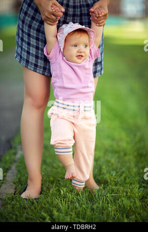 Die Mutter ihr Baby die ersten Schritte barfuß auf dem Gras zu nehmen Stockfoto