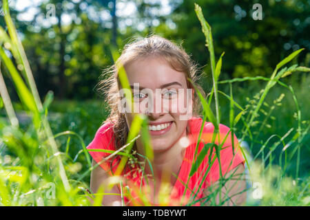 Lächelnde junge Frau liegt auf einer Wiese und blickt in die Kamera Stockfoto