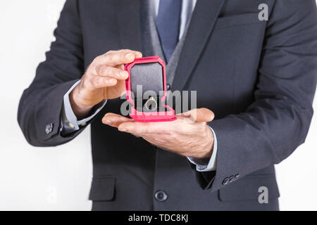 Junger Mann in Anzug mit Krawatte hält eine Box mit Hochzeit Ringe. Zeit für Engagement und Schritt in das Erwachsenenleben. Trauringe als Symbol des glücklichen Lebens Stockfoto