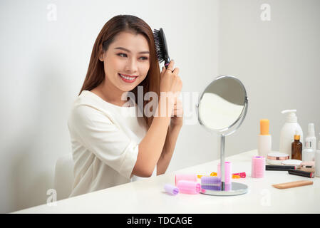 Das Loswerden von Kabelsalat. Schöne junge Frau an ihr Spiegelbild in mirrorand ihr langes Haar bürsten Während am Tisch sitzen Stockfoto