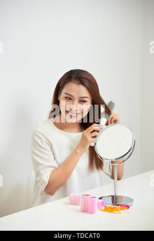 Das Loswerden von Kabelsalat. Schöne junge Frau an ihr Spiegelbild in mirrorand ihr langes Haar bürsten Während am Tisch sitzen Stockfoto