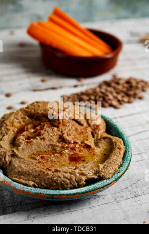 Nahaufnahme von einem hausgemachten Linse hummus gewürzt mit Paprika in einer grünen Keramikplatte auf einem weißen Holzmöbeln im Landhausstil Tisch serviert, und eine Schüssel im Hintergrund Stockfoto