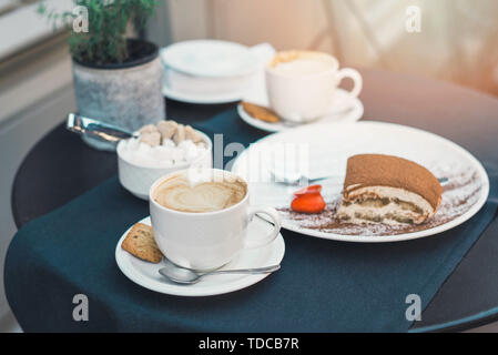 Zwei Tassen Kaffee und Tiramisu auf schwarzem Hintergrund Tabelle mit schönen Latte Art in Herzform. Stockfoto