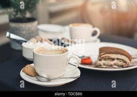 Zwei Tassen Kaffee und Tiramisu auf schwarzem Hintergrund Tabelle mit schönen Latte Art in Herzform. Stockfoto