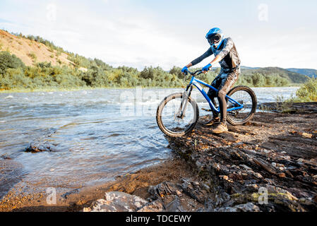 Professionelle gut ausgestattete Radfahrer reiten auf dem felsigen Riverside in den Bergen. Konzept der Freeride- und off road Radfahren Stockfoto