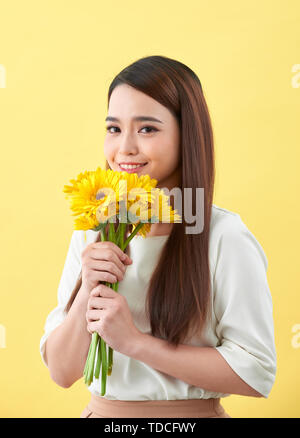 Junge Frau riecht Sonnenblumen auf dem gelben Hintergrund Stockfoto