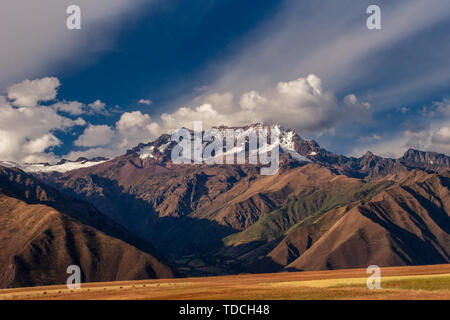 Blick auf die Anden in der Nähe der Stadt Cusco in Peru. Berg mit Schnee bedeckt und dramatische Wolken im blauen Himmel. Stockfoto