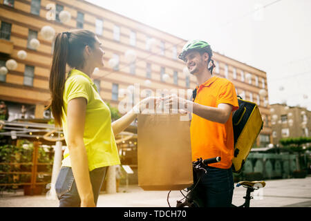 Junger Mann im gelben Trikot, Paket mit Gadgets um an der Hauptstraße der Stadt zu verfolgen. Kurier online App für den Empfang der Zahlung, die Adresse und die Empfänger. Moderne Technologien. Stockfoto