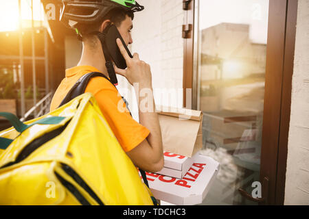 Junger Mann im gelben Trikot liefern Pizza mit Gadgets um an der Hauptstraße der Stadt zu verfolgen. Kurier online App für den Empfang der Zahlung und Versand Adresse. Moderne Technologien. Stockfoto