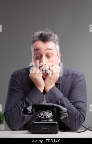 In dem Bestreben, Geschäftsmann an einem Telefon suchen in Angst offenen Mund starrt, als er auf einen wichtigen Anruf mit Kopie Raum über wartet Stockfoto