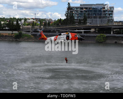 Der Küstenwache aircrew an Bord einer MH-60 Jayhawk Helikopter aus Sektor Columbia River senkt eine Aviation überleben Techniker in den Willamette River in der Rose Festival in Portland, Erz, 8. Juni 2019. Die flugzeugbesatzung, ließ eine Schulung Dummy in den Fluss ein Verwertungsverfahren für die tausenden von Schaulustigen an der Rose Festival Flotte Woche zu demonstrieren. U.S. Coast Guard Foto von Petty Officer 3. Klasse Trevor Lilburn. Stockfoto